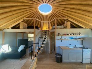 the inside of a yurt with stairs leading up to an open kitchen and living area