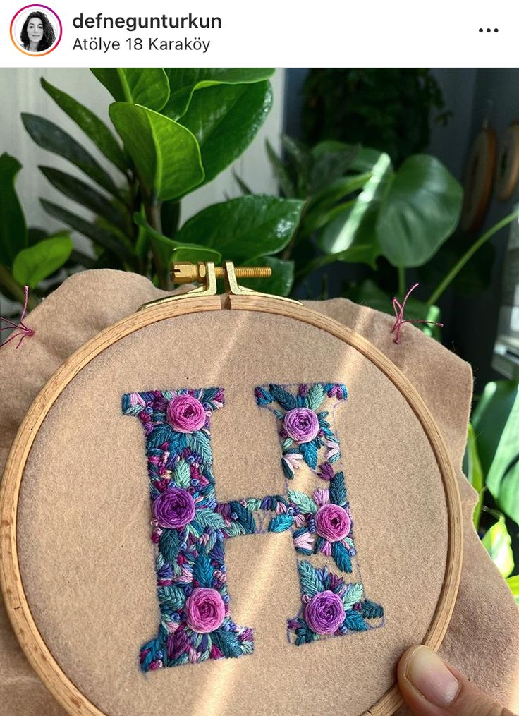 a hand embroidered letter h with flowers on it in front of a potted plant