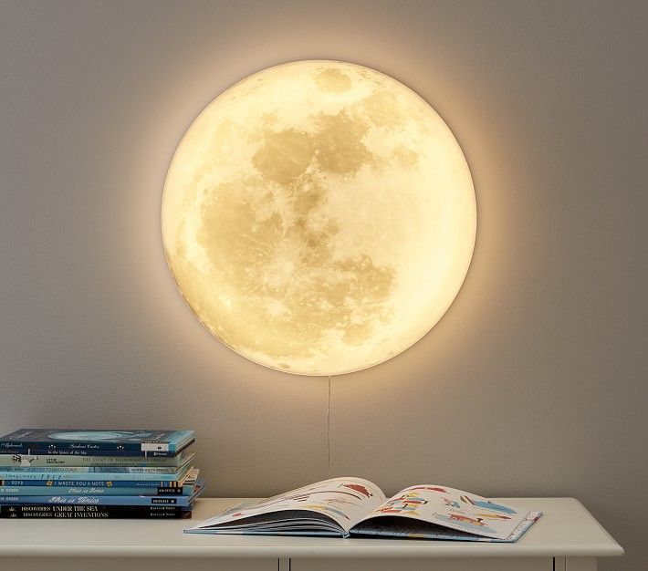 the moon is lit up above some books on a white shelf in front of a gray wall