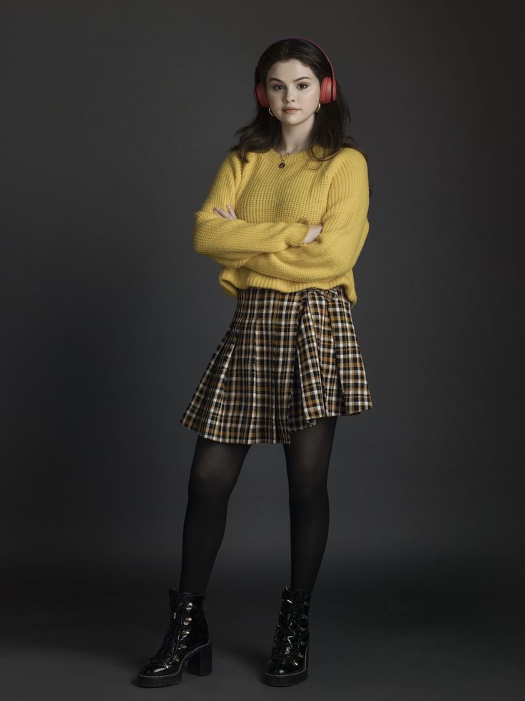 a woman in yellow sweater and plaid skirt standing with her arms crossed