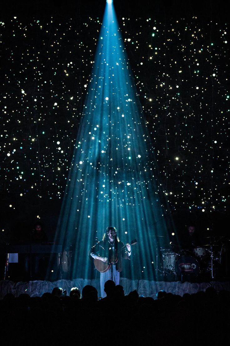 a person standing on stage in front of a light show with bright beams coming from the ceiling