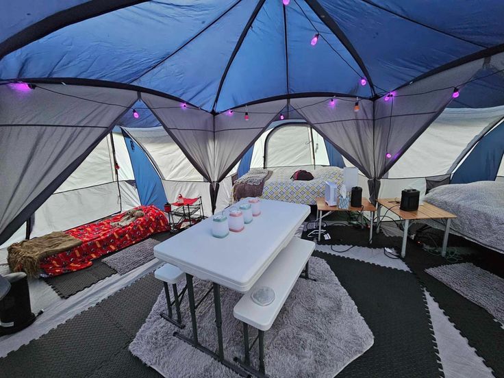 the inside of a tent with several beds and tables in it, all lit up by purple lights