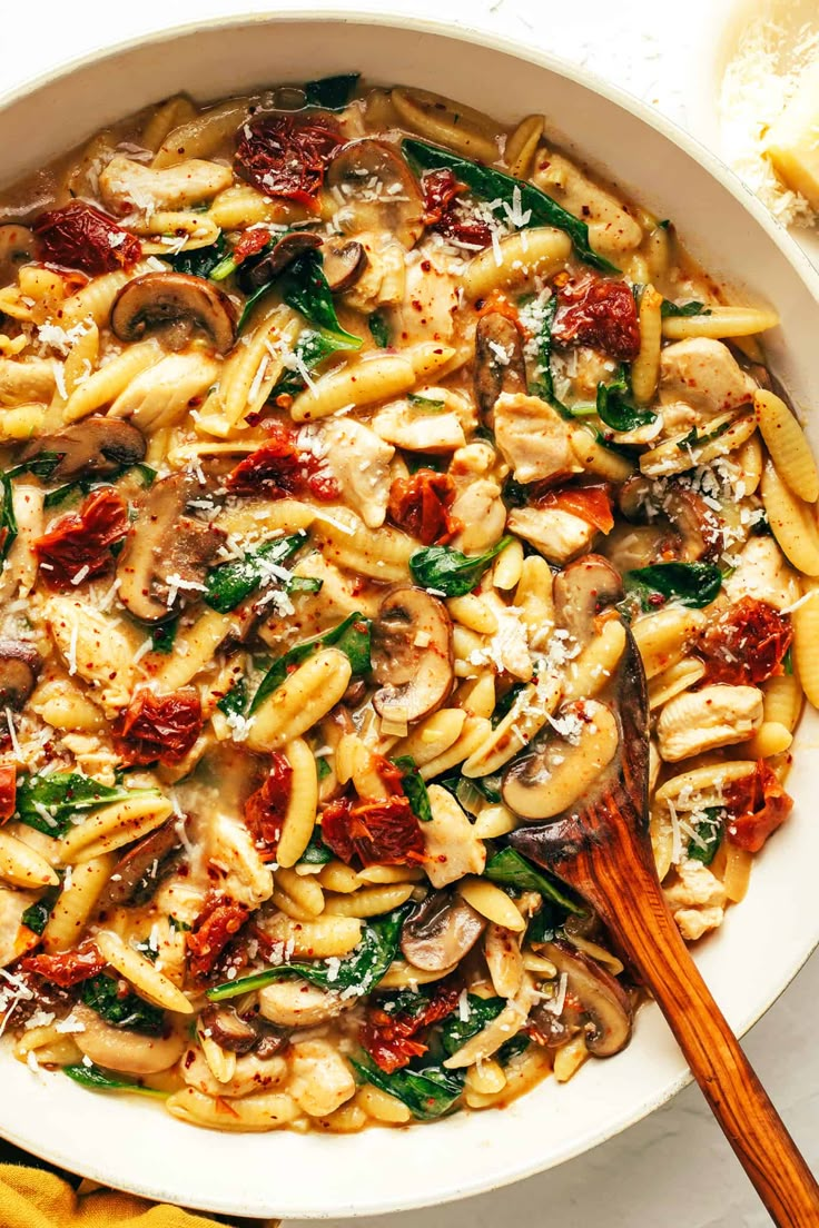 pasta with mushrooms, spinach and sun dried tomatoes in a white bowl next to bread