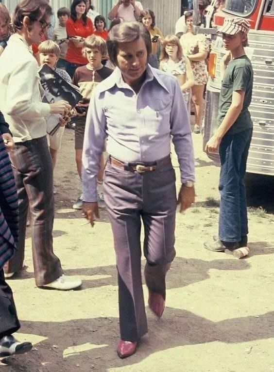 an old photo of a man walking down the street with people watching from behind him