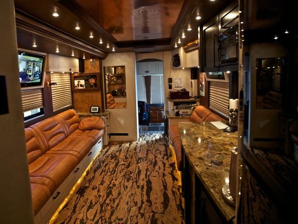 the inside of a bus with couches, tables and televisions on it's walls