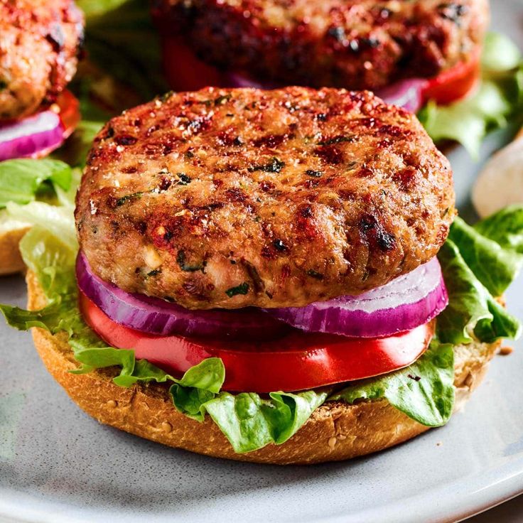 two burgers with lettuce, tomato and onion on a white platter