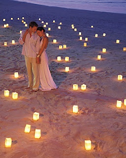 a man and woman standing in the sand surrounded by lit candles