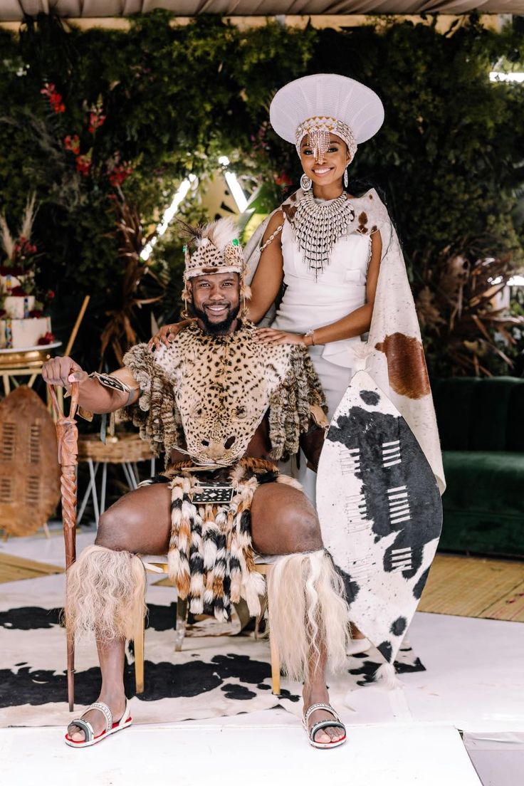 a man and woman dressed in native garb sitting on a chair with an animal costume