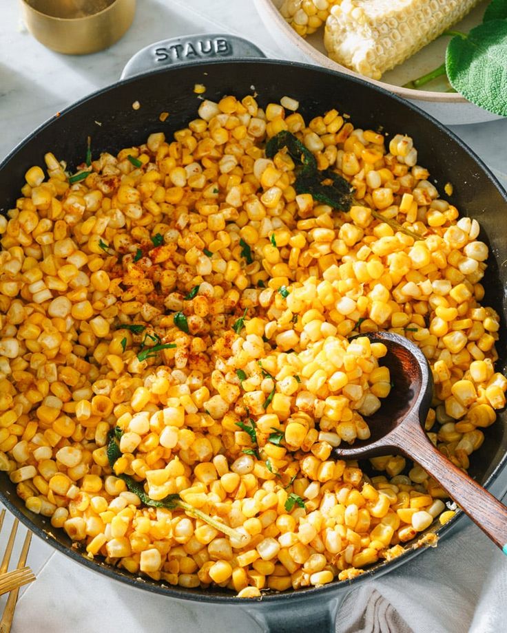 corn is being cooked in a skillet with a wooden spoon next to other dishes