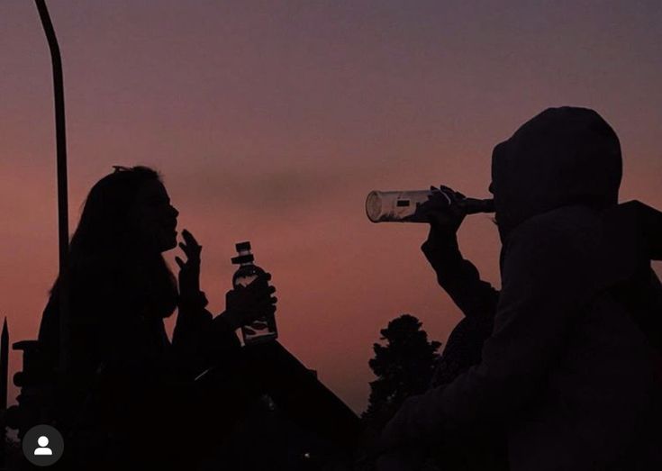 two people drinking from bottles at dusk with the sun setting in the sky behind them