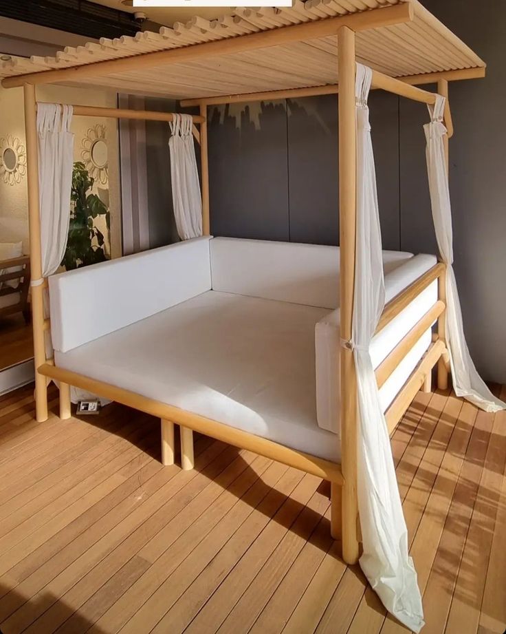 a canopy bed with white sheets and curtains on top of wooden flooring in a bedroom