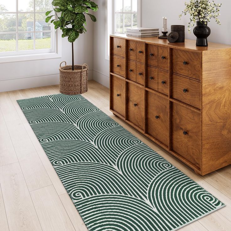 a green and white area rug on a wooden floor next to a dresser with a potted plant