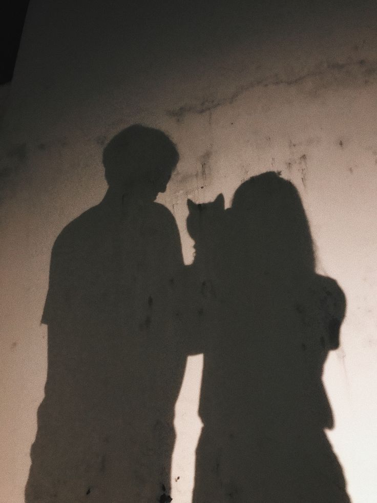 two people standing next to each other with a cat in their hand and shadow on the wall