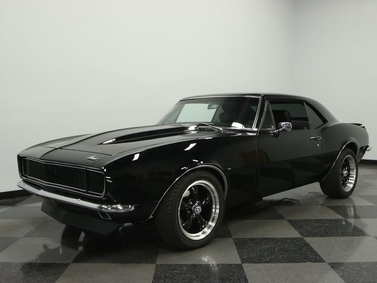 a black muscle car is parked in a room with checkered flooring and white walls