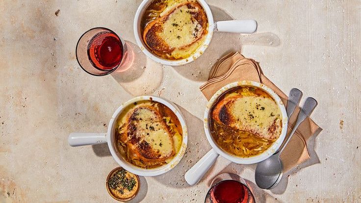 three bowls filled with food on top of a table next to two glasses of wine