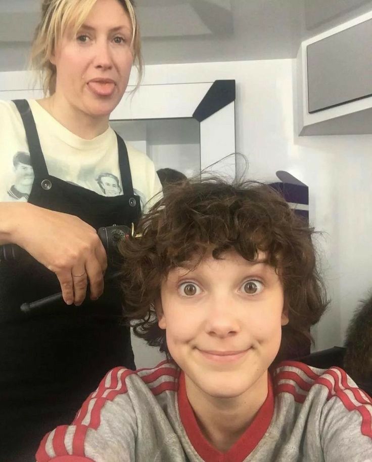 a young boy getting his hair cut by an older woman in front of the mirror