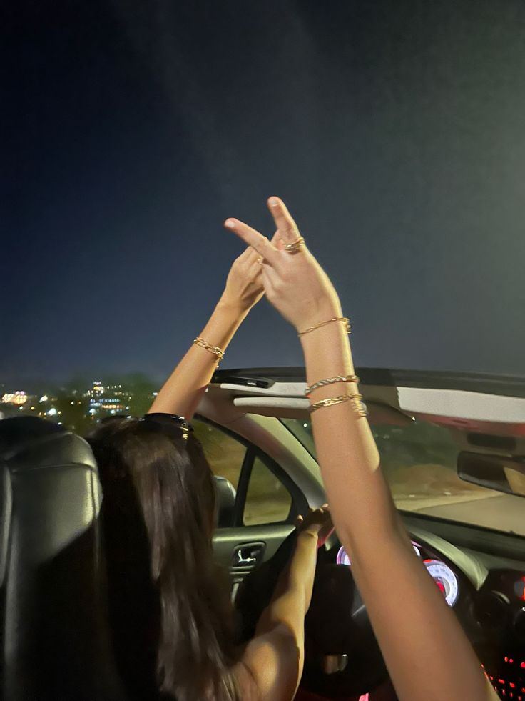 two people sitting in a car making the v sign with their hands while they are driving at night