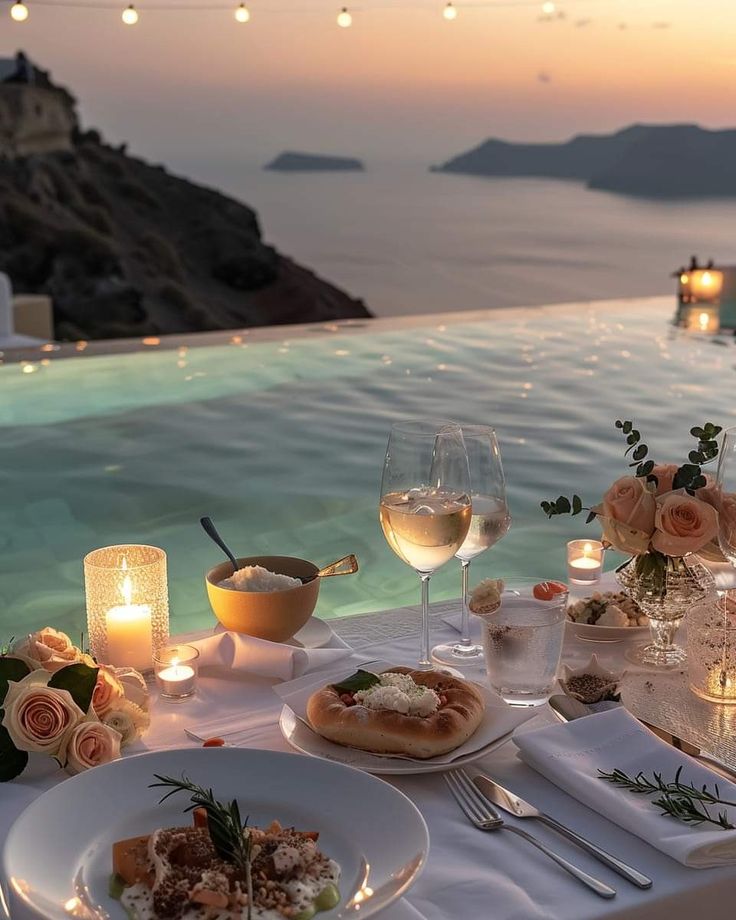 a table with food and wine next to an outdoor swimming pool at sunset or sunrise