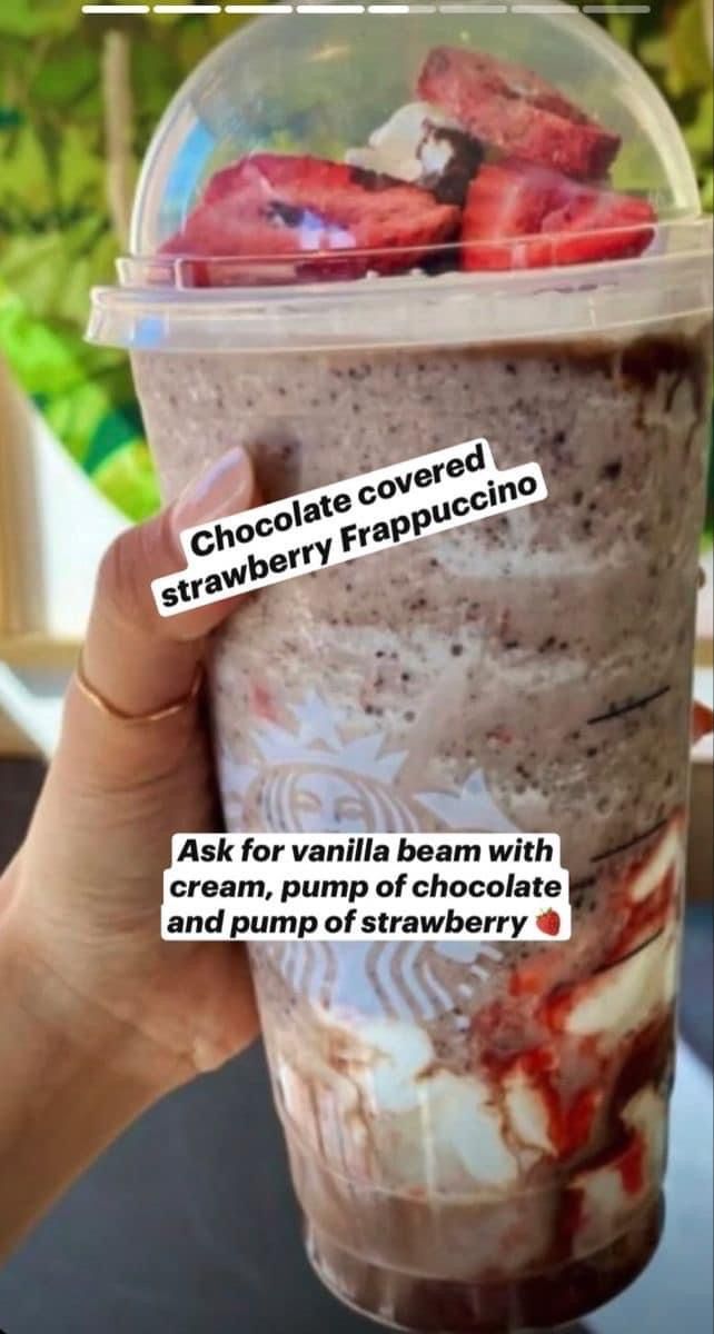 a person holding up a cup with strawberries in it and the words chocolate covered strawberry frappuccino