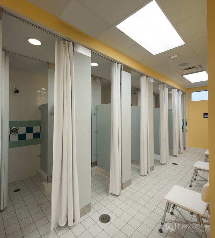 an empty bathroom with several stalls and white curtains on the walls, in front of a tiled floor