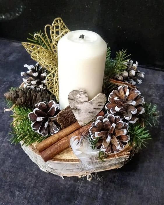 a white candle sitting on top of a wooden bowl filled with pine cones and cinnamons