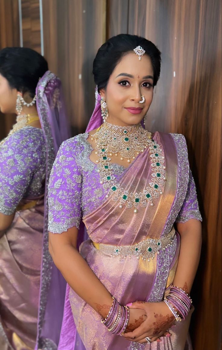 a woman in a purple and gold sari standing next to another woman with her hands on her hips