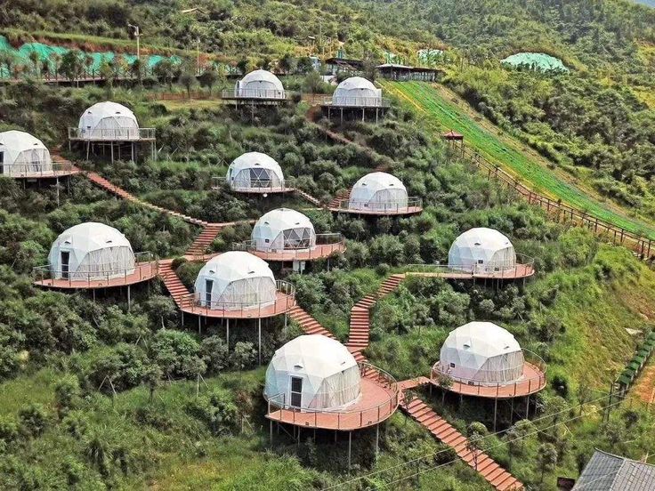 several large white domes sitting on top of a lush green hillside covered in trees and grass