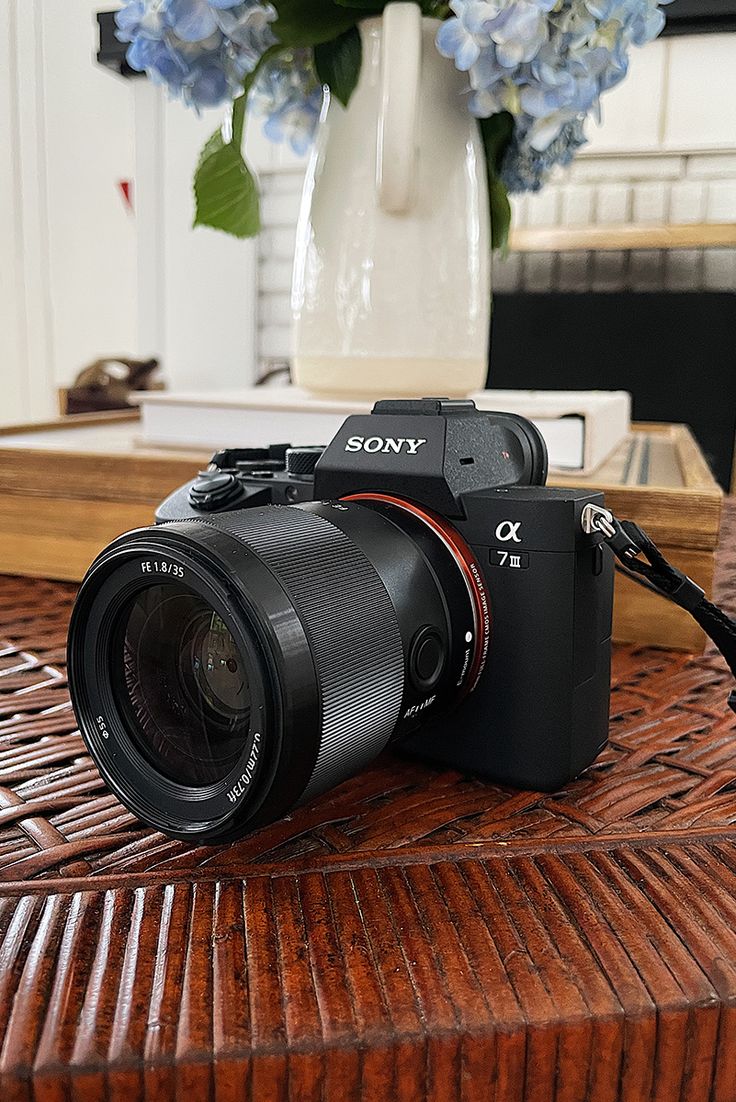 a camera sitting on top of a wooden table next to a vase with blue flowers