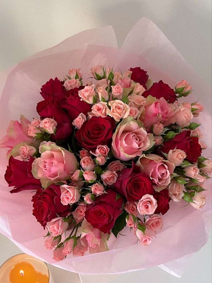 a bouquet of pink and red roses next to an orange candle