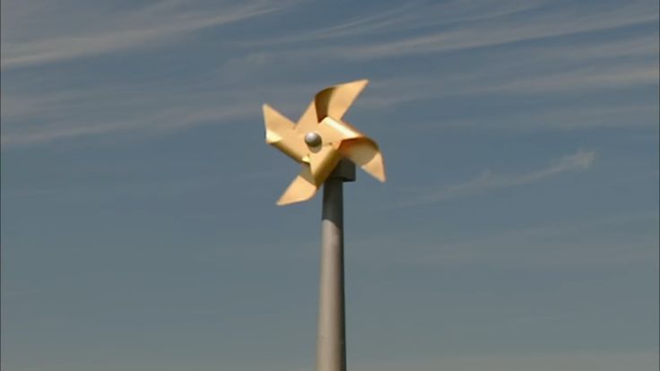 a tall metal pole with a yellow flower on it's top and blue sky in the background