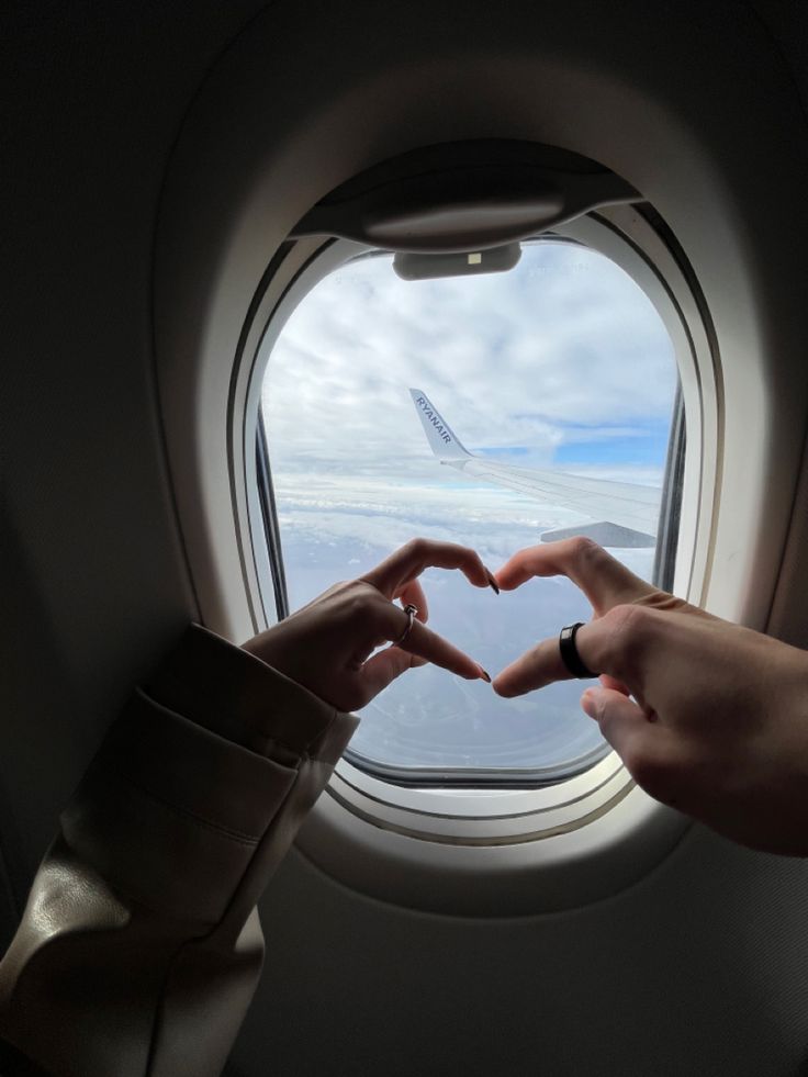 two people making a heart shape with their hands in front of an airplane window while flying