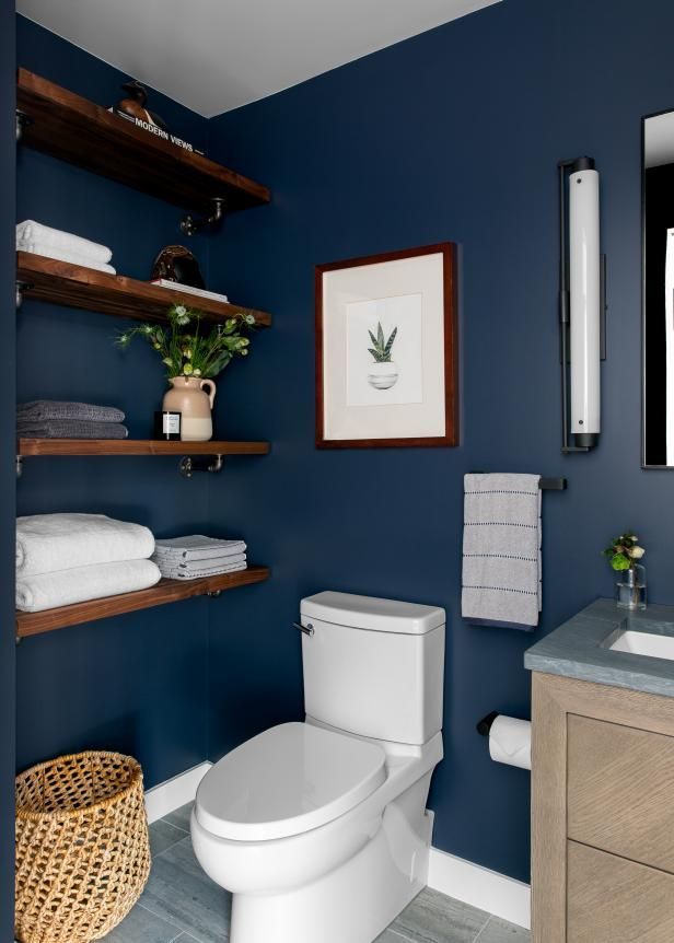 a white toilet sitting next to a wooden cabinet in a bathroom with blue walls and shelving