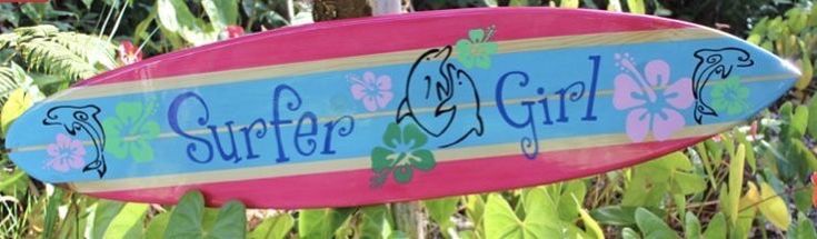 a pink and blue surfboard with the words surfer girl on it hanging from a tree