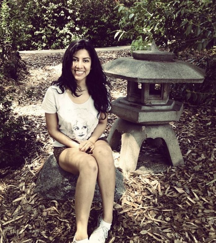 a woman sitting on top of a rock next to a small stone lantern in the woods