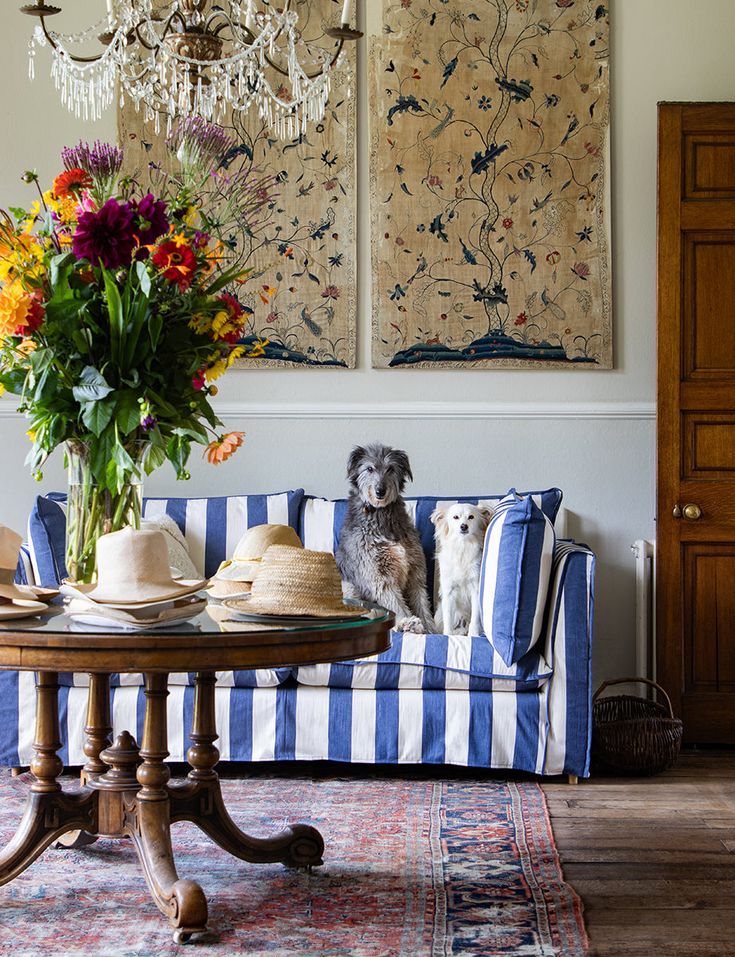 a dog sitting on a blue and white striped couch next to a vase with flowers