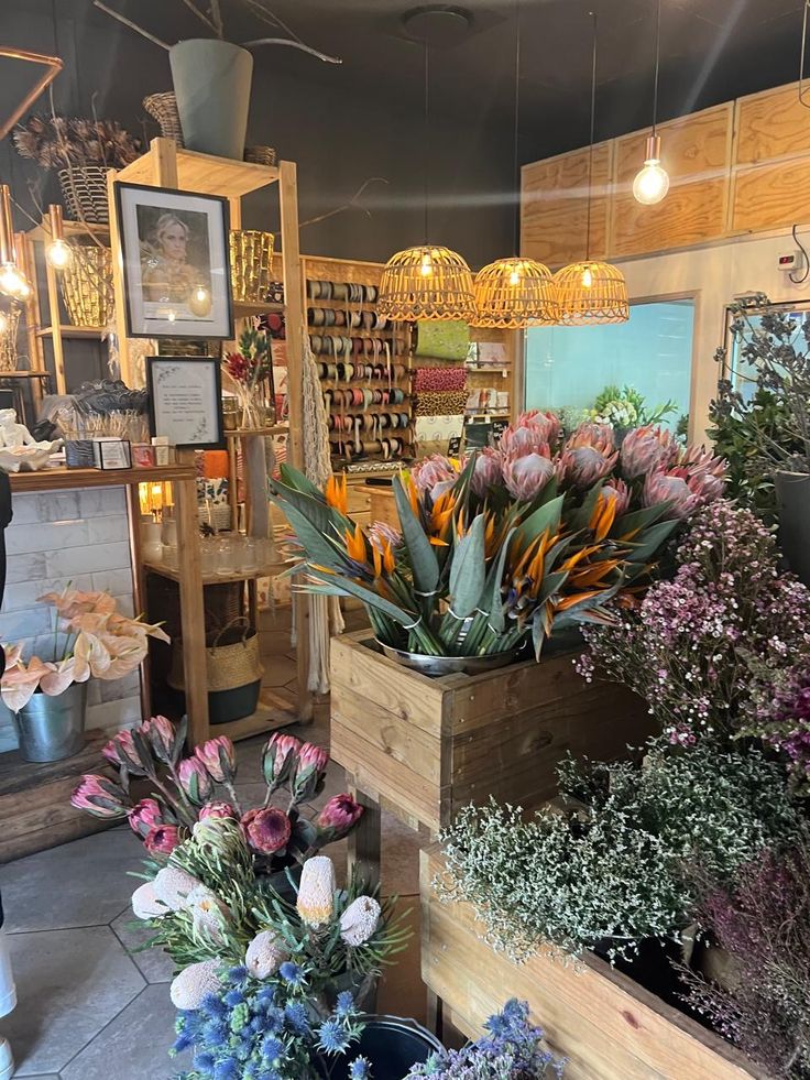 flowers are sitting in wooden containers on the floor at a flower shop with hanging lights above them