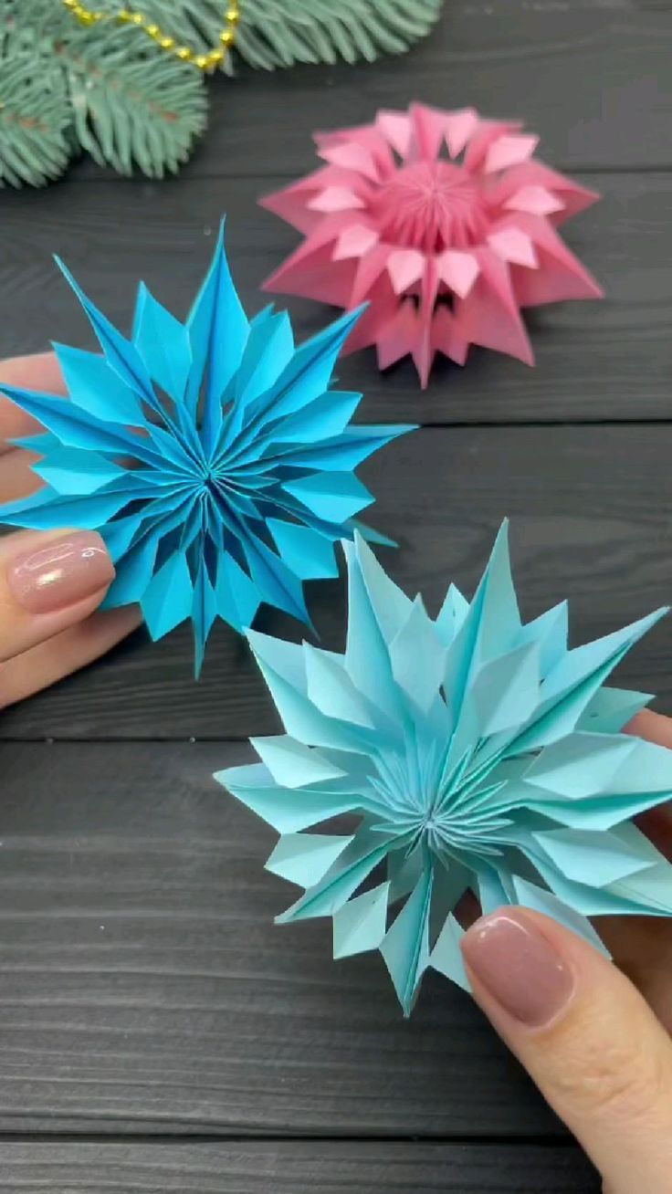 three origami flowers are being held by someone's hands on a table