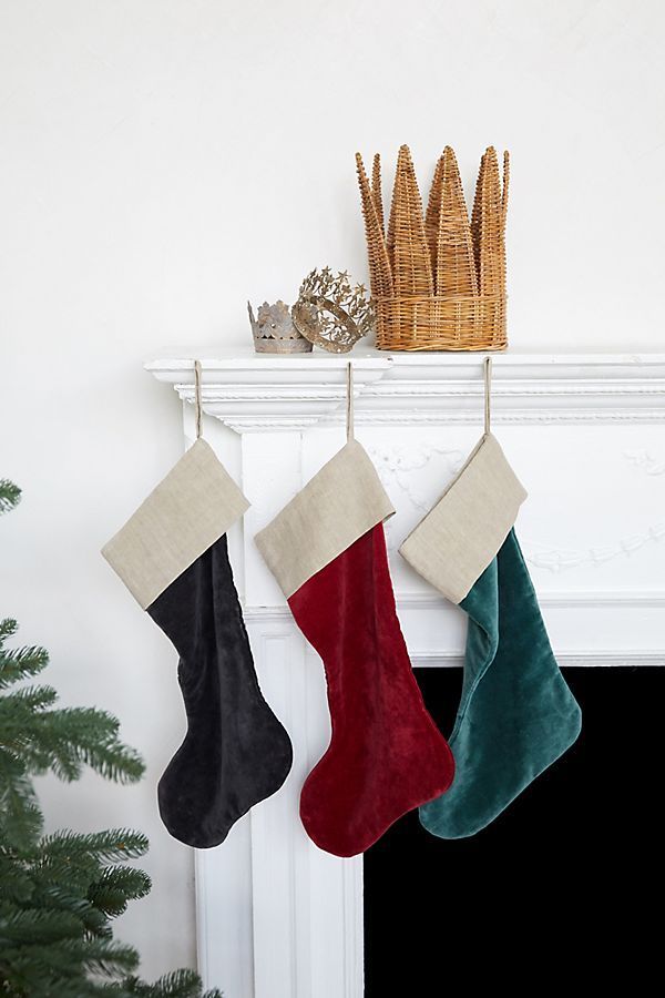 three christmas stockings hanging from a mantel above a fireplace with a basket and tree in the background