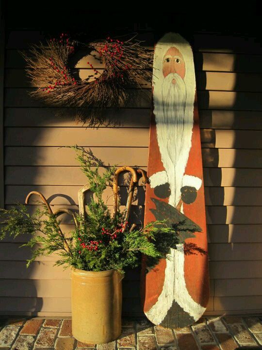 a surfboard with a santa clause on it next to a potted plant and wreath