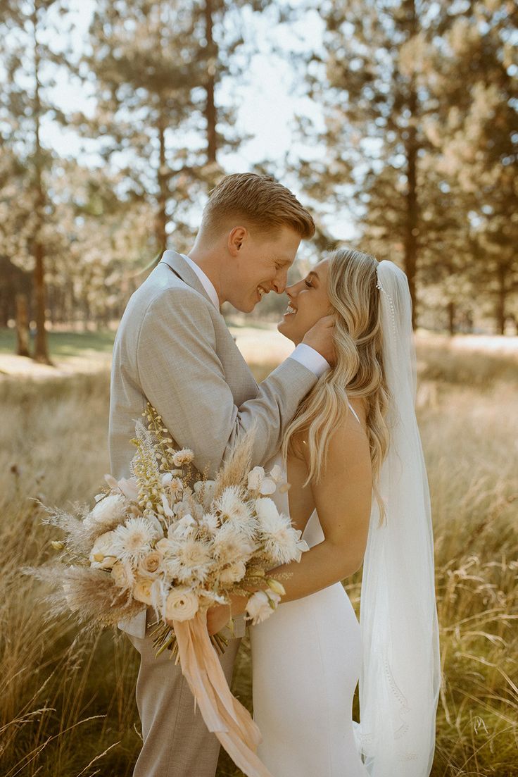 a bride and groom are standing in the grass with their heads close to each other