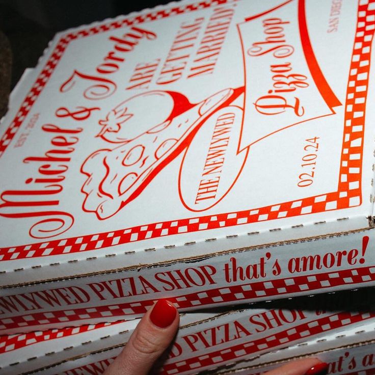 three pizza boxes stacked on top of each other with one person's hand pointing at them