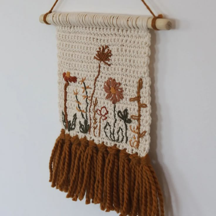 a crocheted wall hanging with flowers and crosses on the front, attached to a white wall