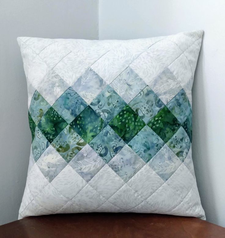 a green and white quilted pillow sitting on top of a wooden table next to a wall