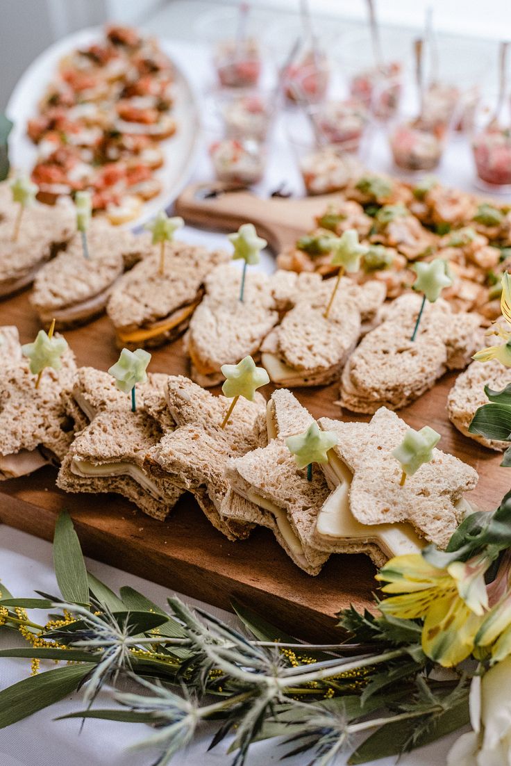 a wooden cutting board topped with lots of food next to plates filled with desserts