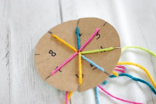 a clock made out of twine on top of a white wooden table with colorful thread