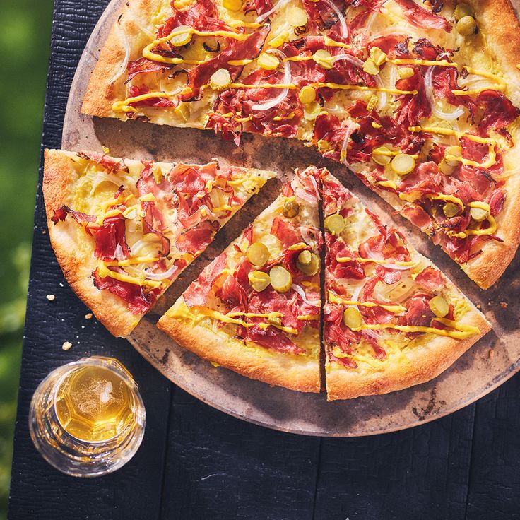 a pizza sitting on top of a wooden table next to a glass of beer and two glasses