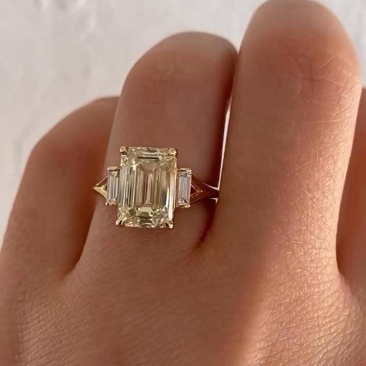 a woman's hand holding an emerald and diamond engagement ring in yellow gold with baguets