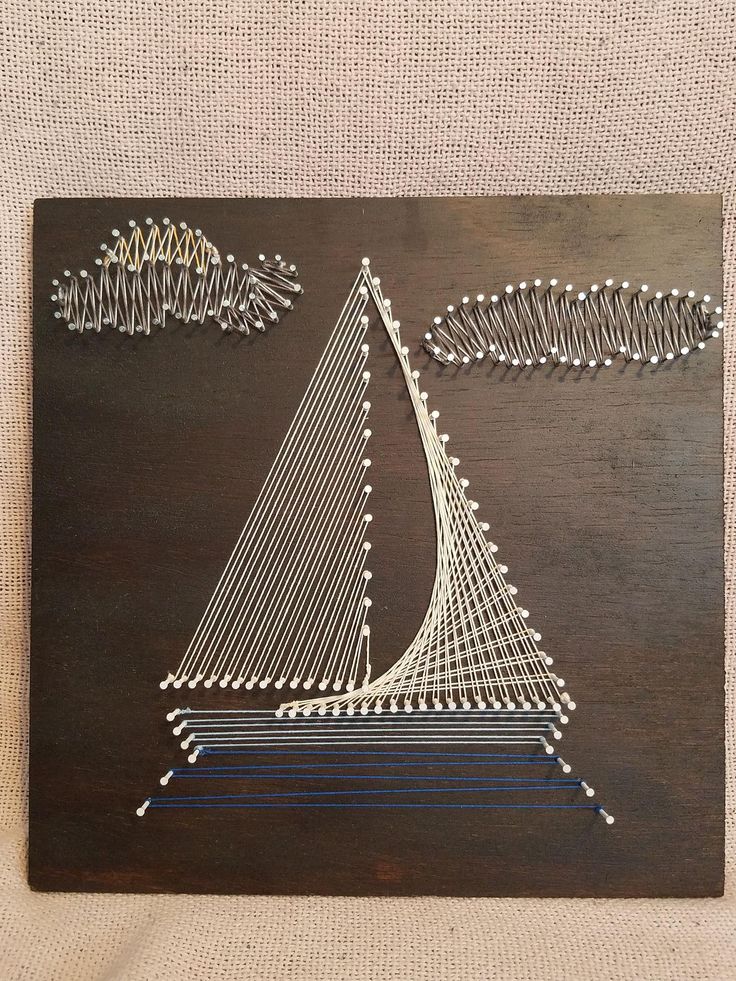 a piece of art that looks like a sailboat on a wooden board with string work