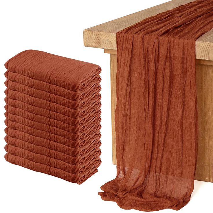 a stack of orange towels sitting on top of a wooden bench next to a pile of red cloth