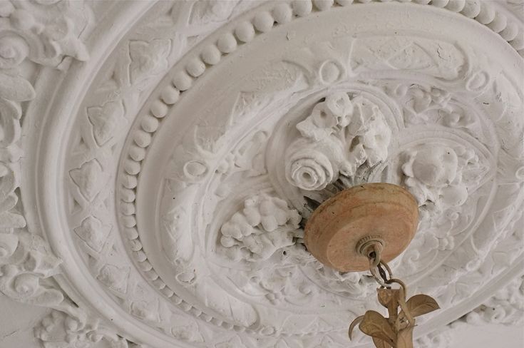 an ornately decorated ceiling light fixture in a white room with intricate carvings on the walls